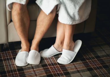 Feet of a man and a woman in Slippers close-up. A young couple in dressing gowns are sitting on a sofa or chair.